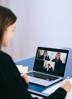 A woman participates in a virtual meeting with colleagues via video call on a laptop.